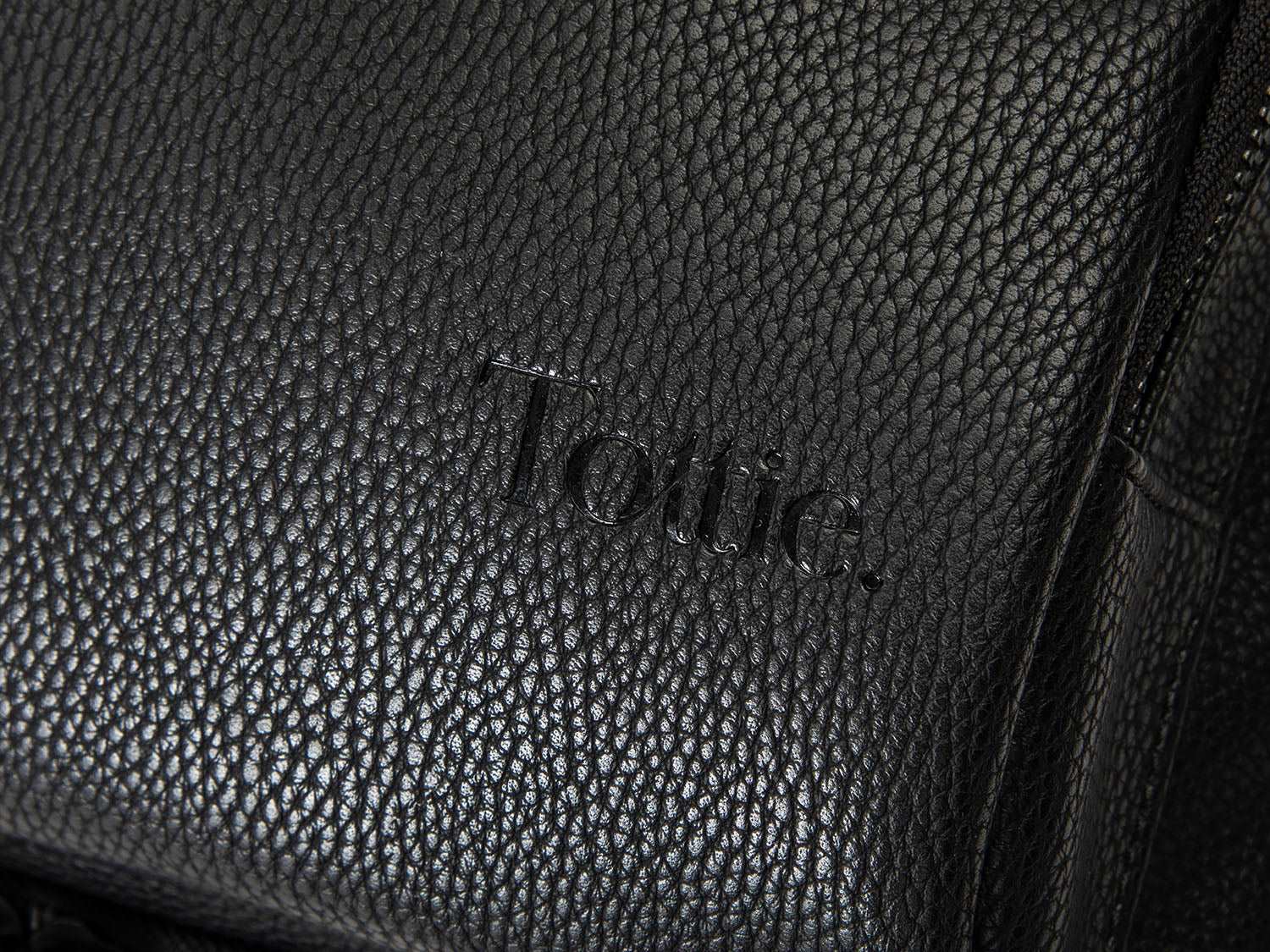 Close-up of the Tottie logo on a black leather nappy backpack