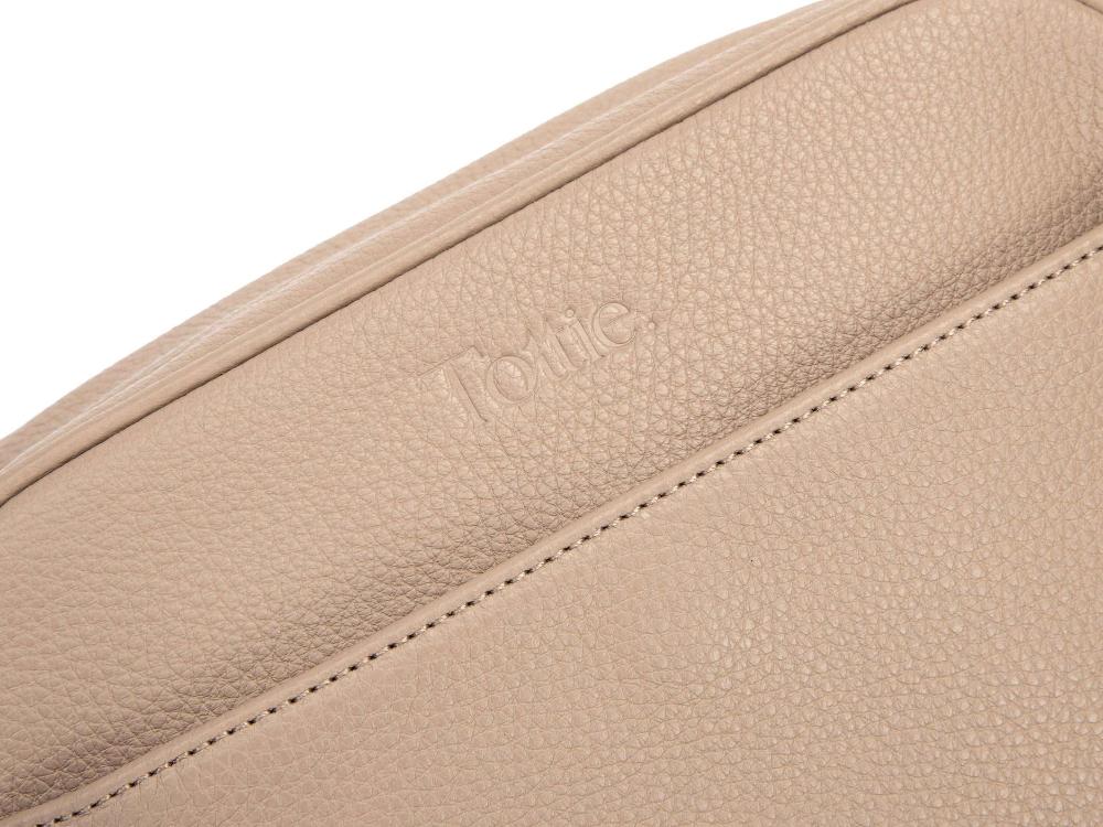  close-up of the front of a stone-colored leather crossbody bag. The brand name "Tottie" is embossed on the leather.