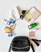 items from a black leather crossbody bag laid out in white background