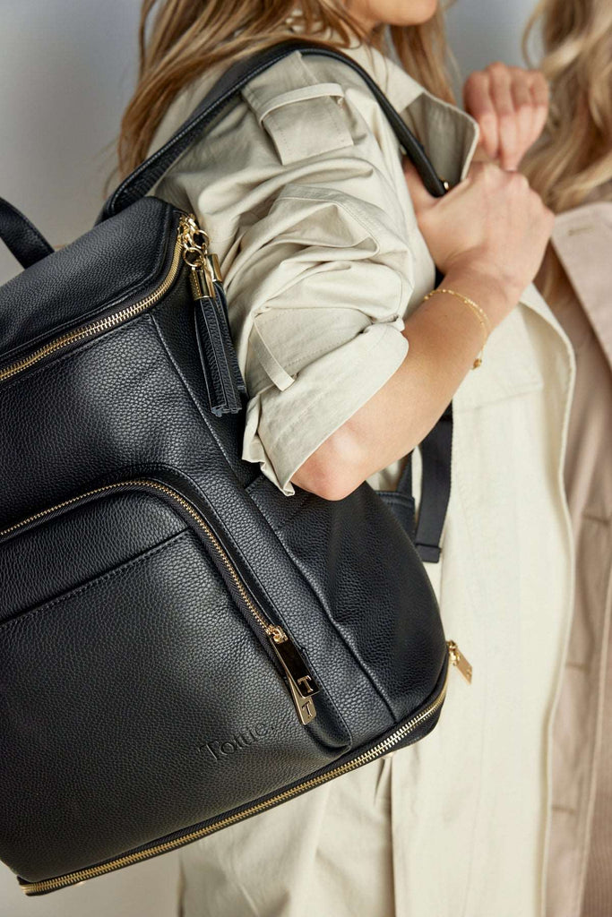 A woman carries a black leather baby bag backpack