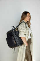 A woman carries a black leather baby bag backpack