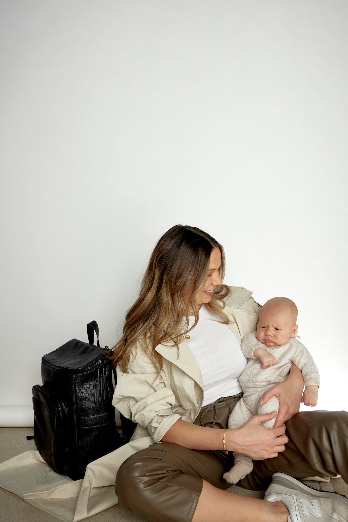 Woman sitting, carrying a baby and wearing a black nappy backpack from Tottie