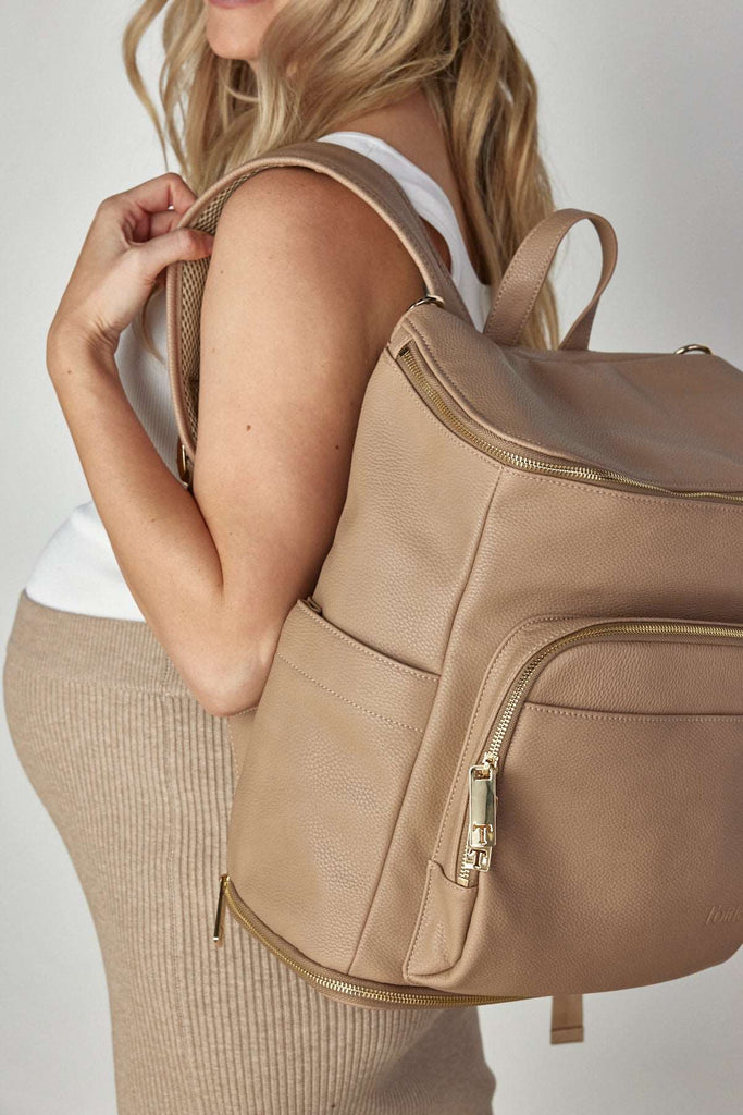 A pregnant woman carrying a stone colour leather baby backpack