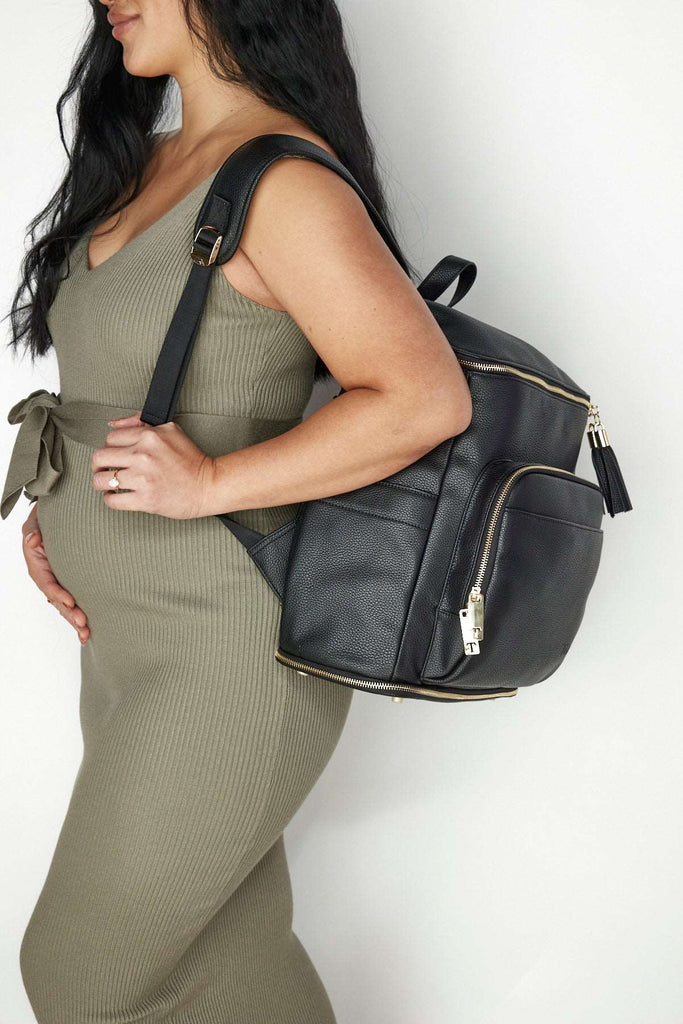 A pregnant woman wearing a black leather baby backpack