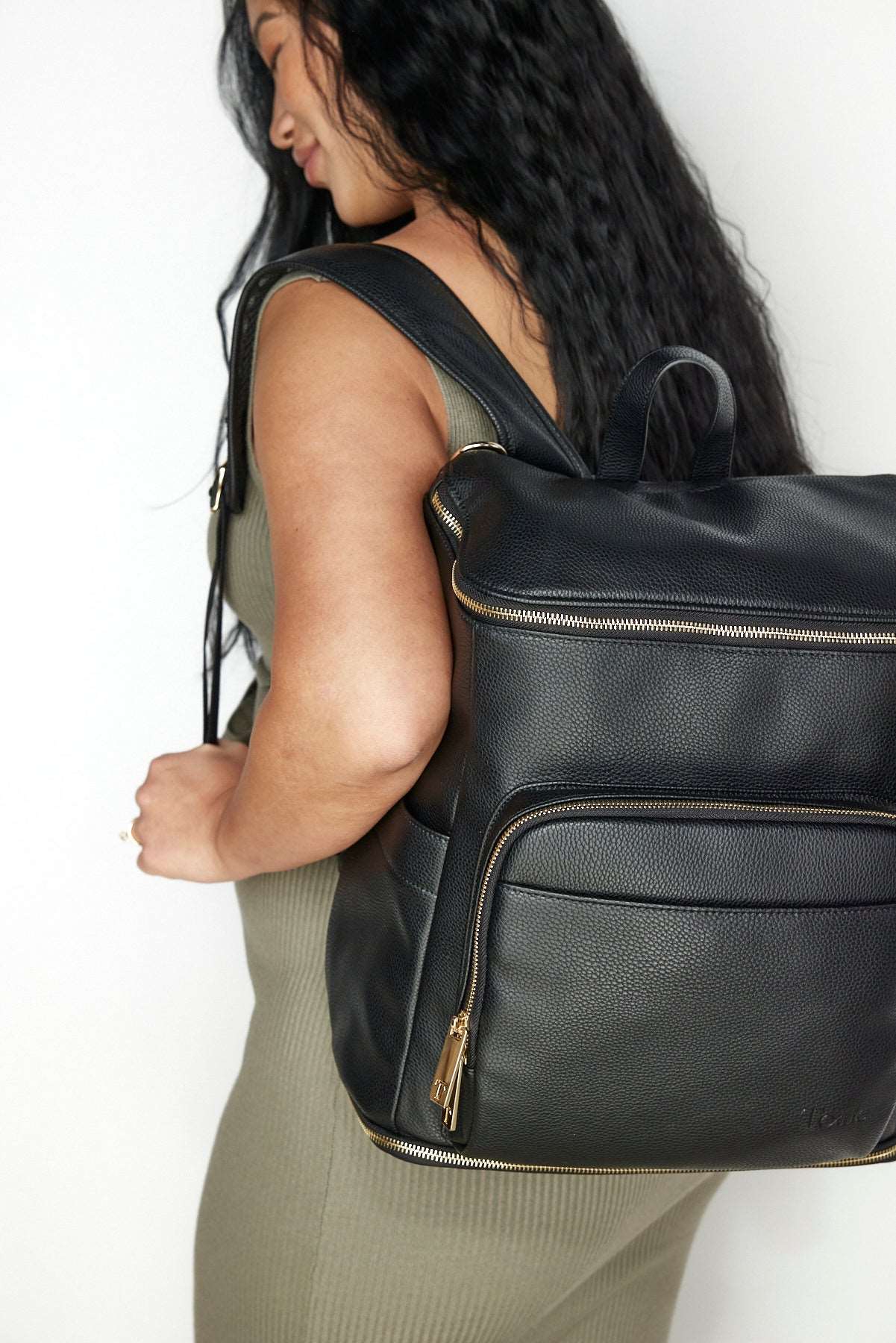 A pregnant woman wearing a black leather baby backpack