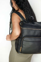 A pregnant woman wearing a black leather baby backpack