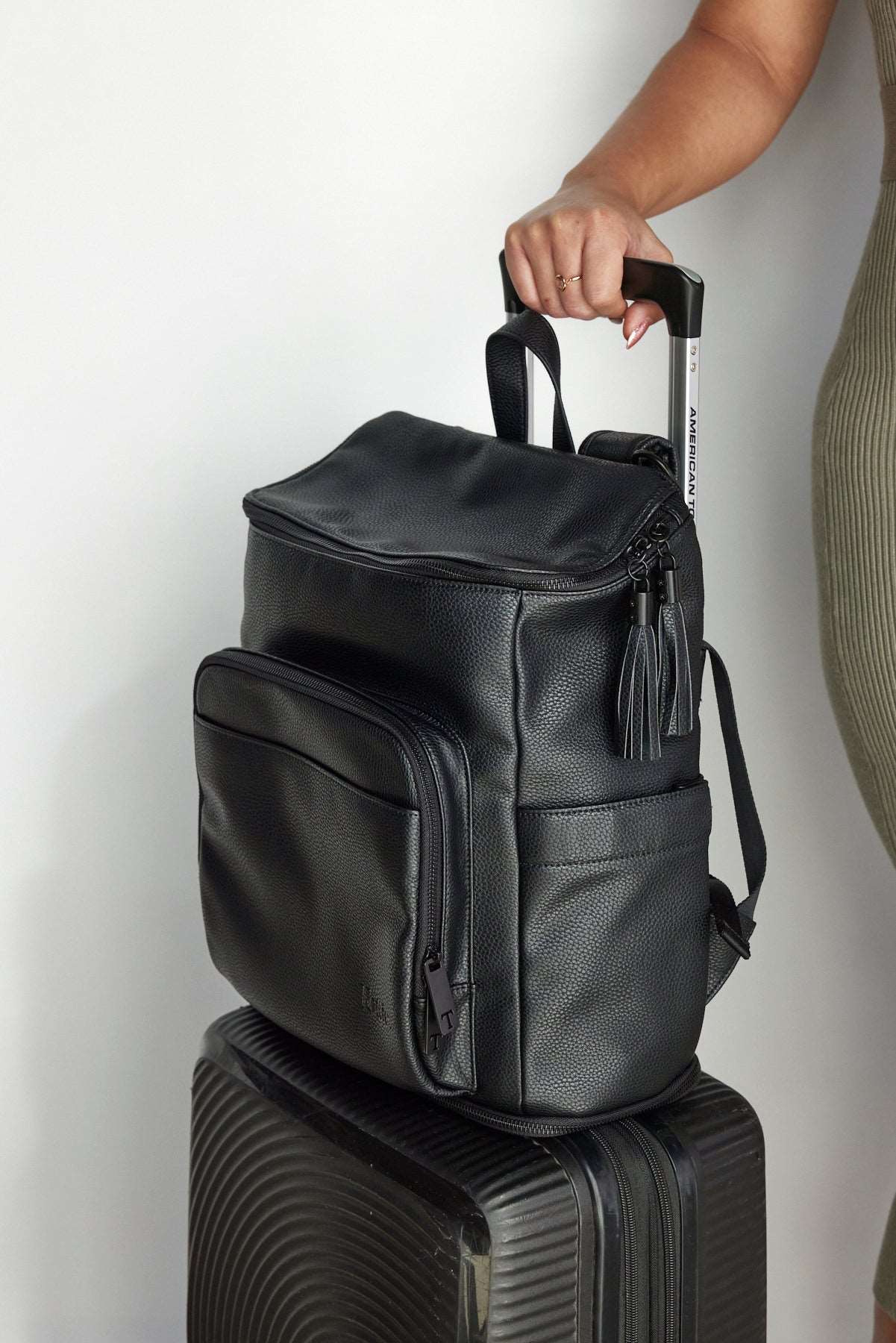 A woman holds a suitcase and a black leather baby backpack