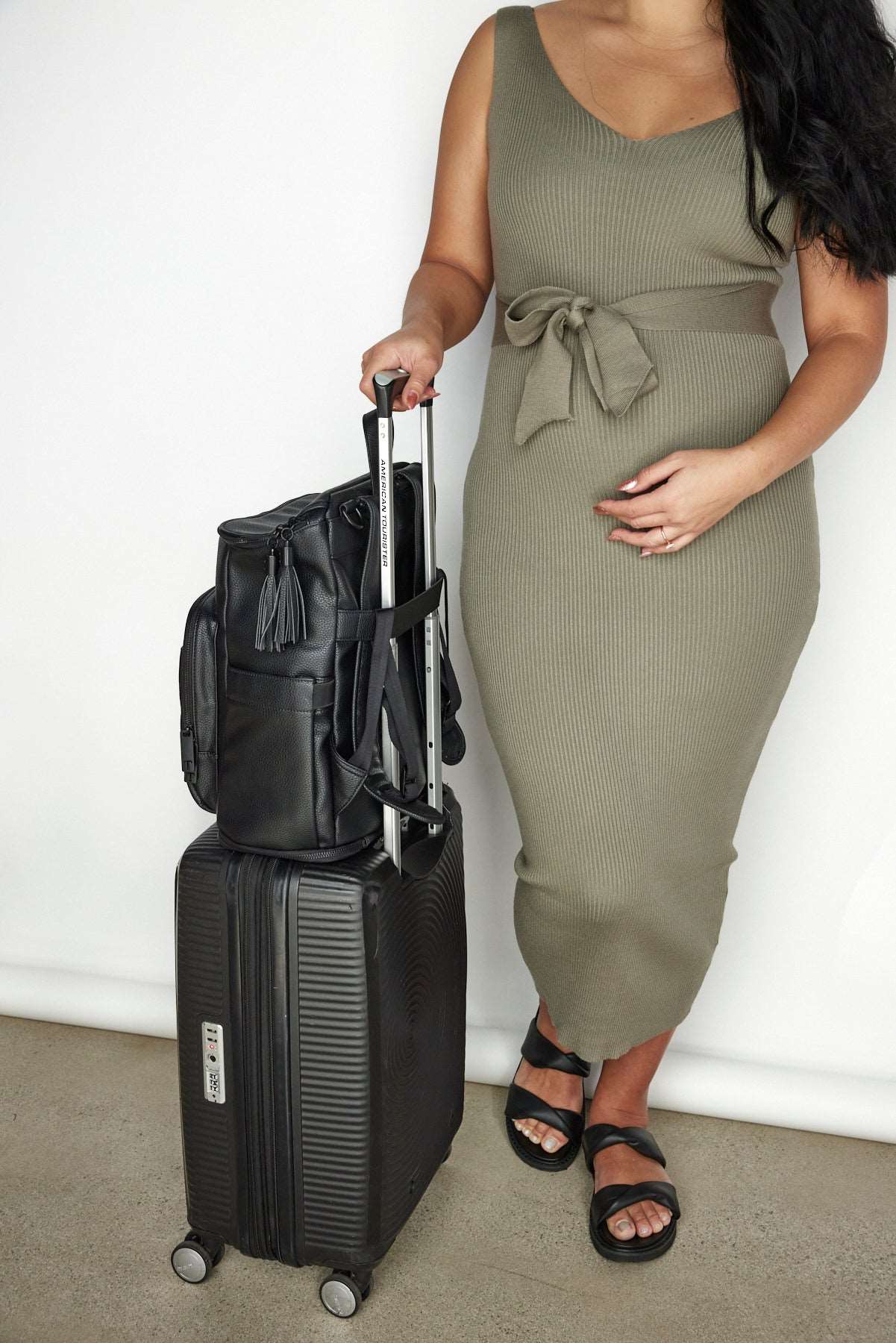 Pregnant woman with black luggage, carrying a black nappy backpack on top