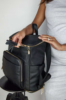 A woman holds a black leather baby bag backpack