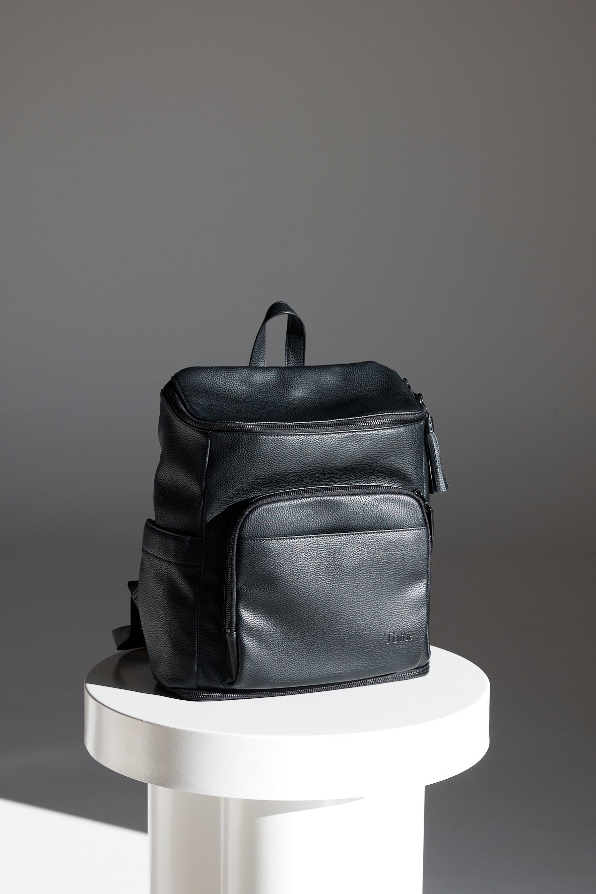 A beautiful photo of a black leather nappy backpack from Tottie with a black zipper.