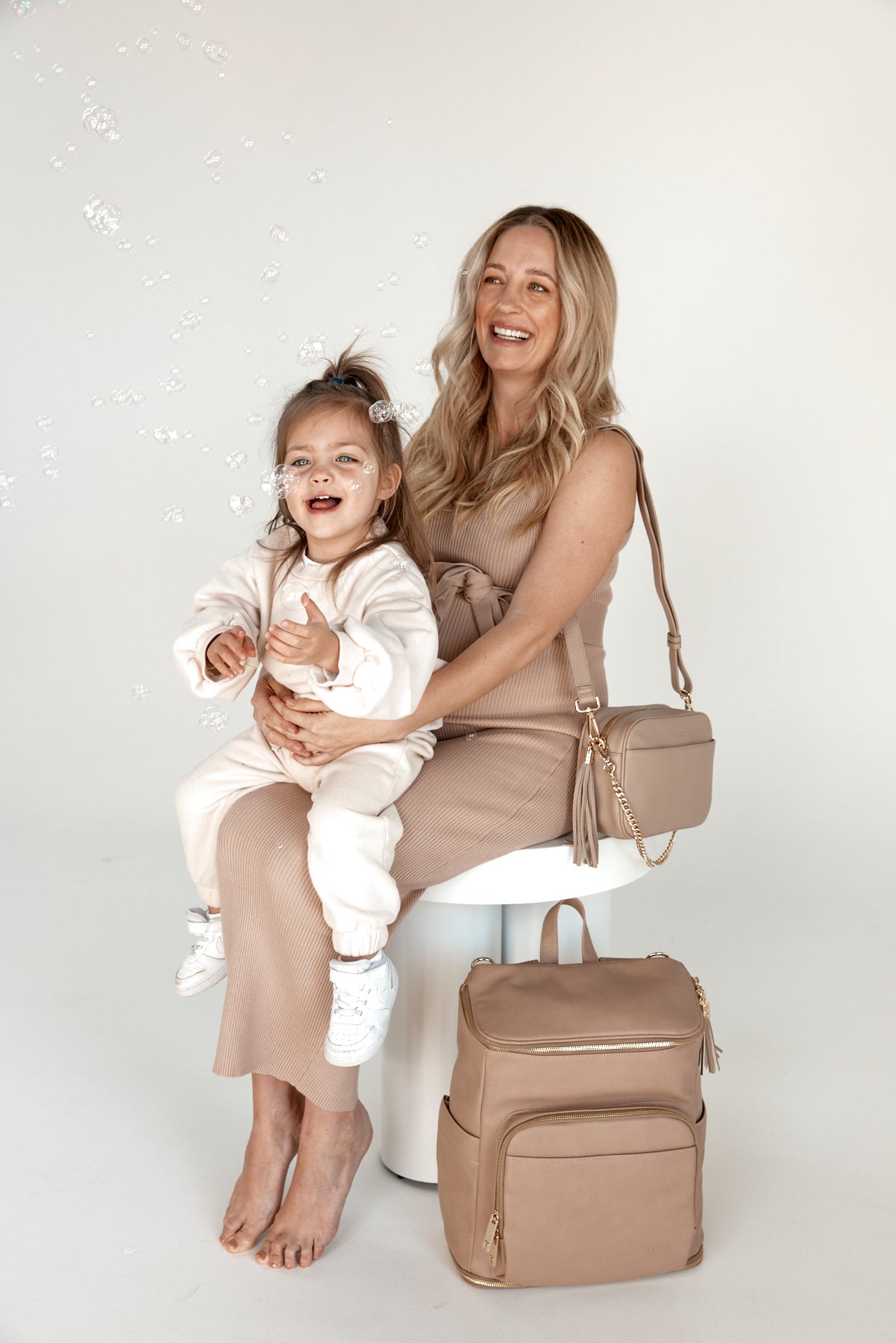 a pregnant woman holding her child and carrying a bestie crossbody bag with a baby backpack beside her