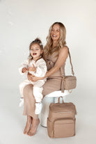 a pregnant woman holding her child and carrying a bestie crossbody bag with a baby backpack beside her