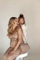 a pregnant woman and a child on her back while carrying a bestie crossbody bag