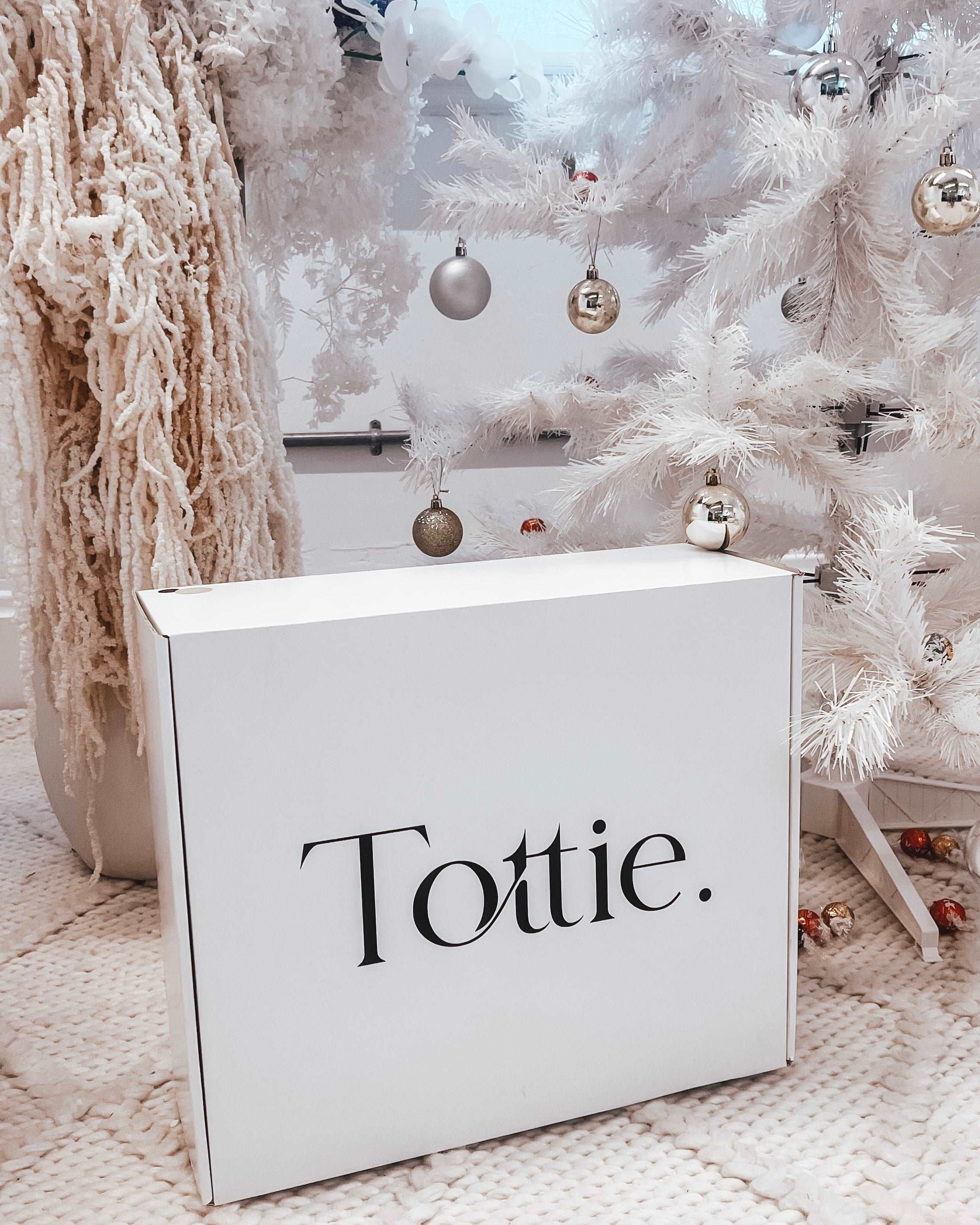 a white box of Tottie goodies under a white Christmas tree