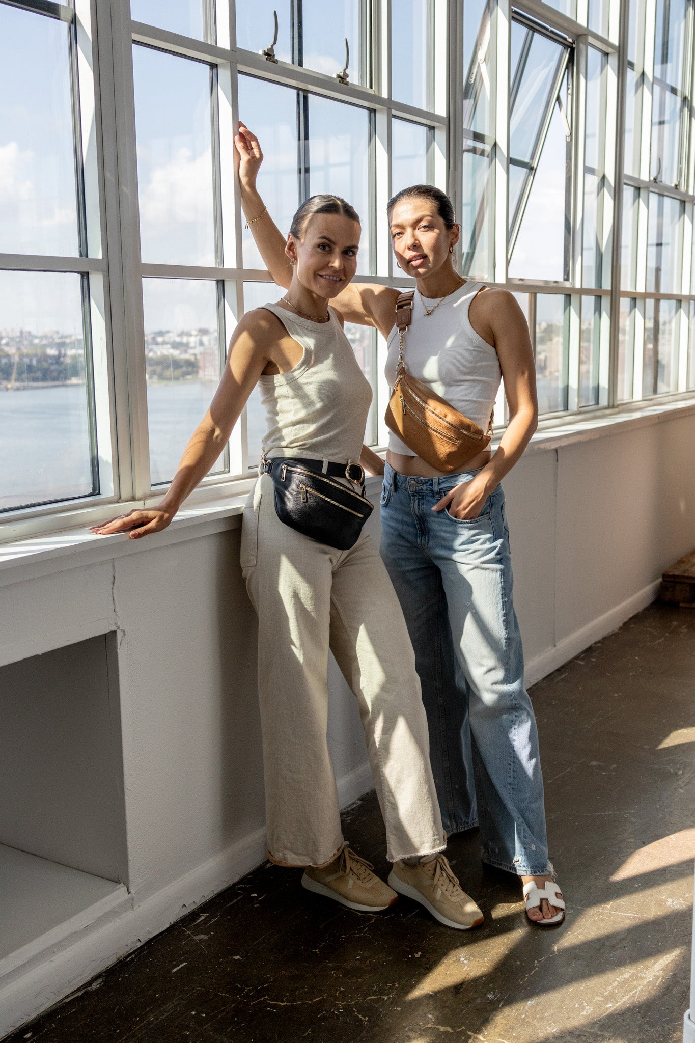 Two women wearing white tops and carrying two bum bags from Tottie: one black and one tan.