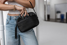 Woman showing a black crossbody bag with black hardware from Tottie, inserting her phone into the bag