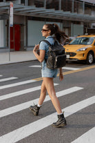 Woman crossing the street in stylish boots, carrying a black nappy backpack with gold hardware