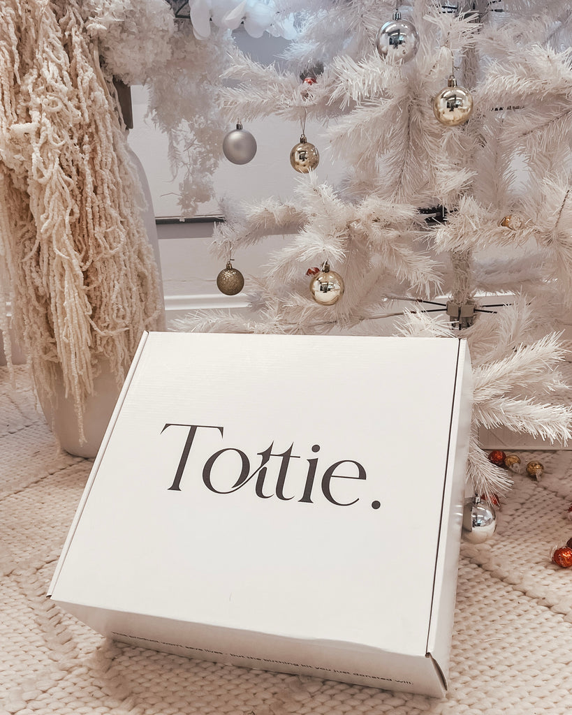 a white box of Tottie goodies under a white Christmas tree